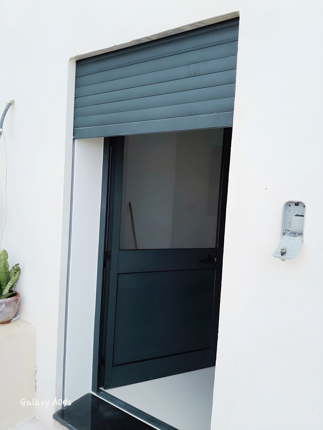 Volet roulant gris entrouvert devant une porte vitrée